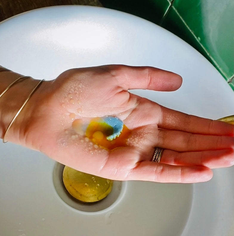 Hand holding a colorful mixture of oils with a sink in the background