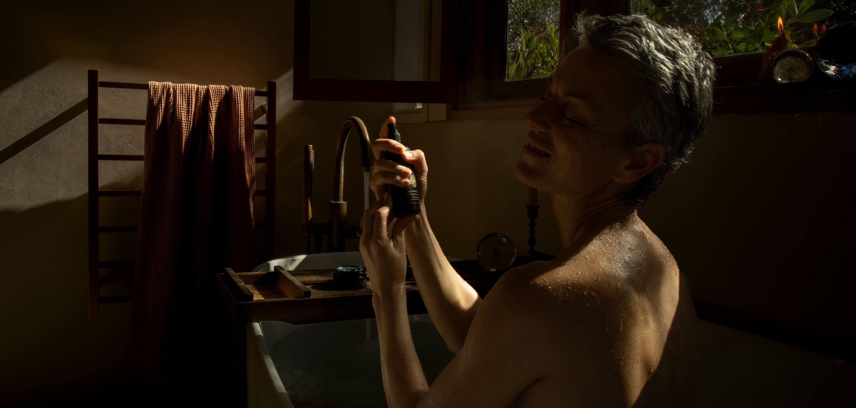 Person spraying a facial mist in a dimly lit bathroom.