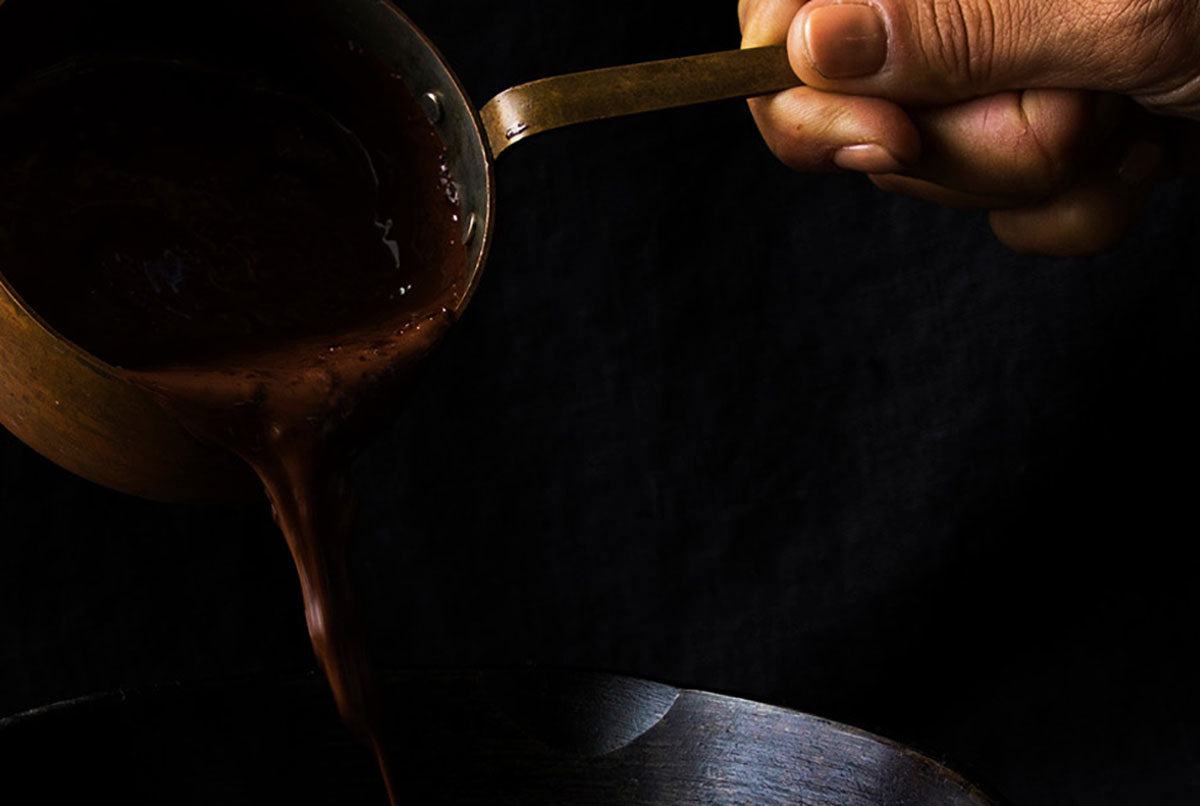 Hand holding a spoon with dark liquid against a dark background
