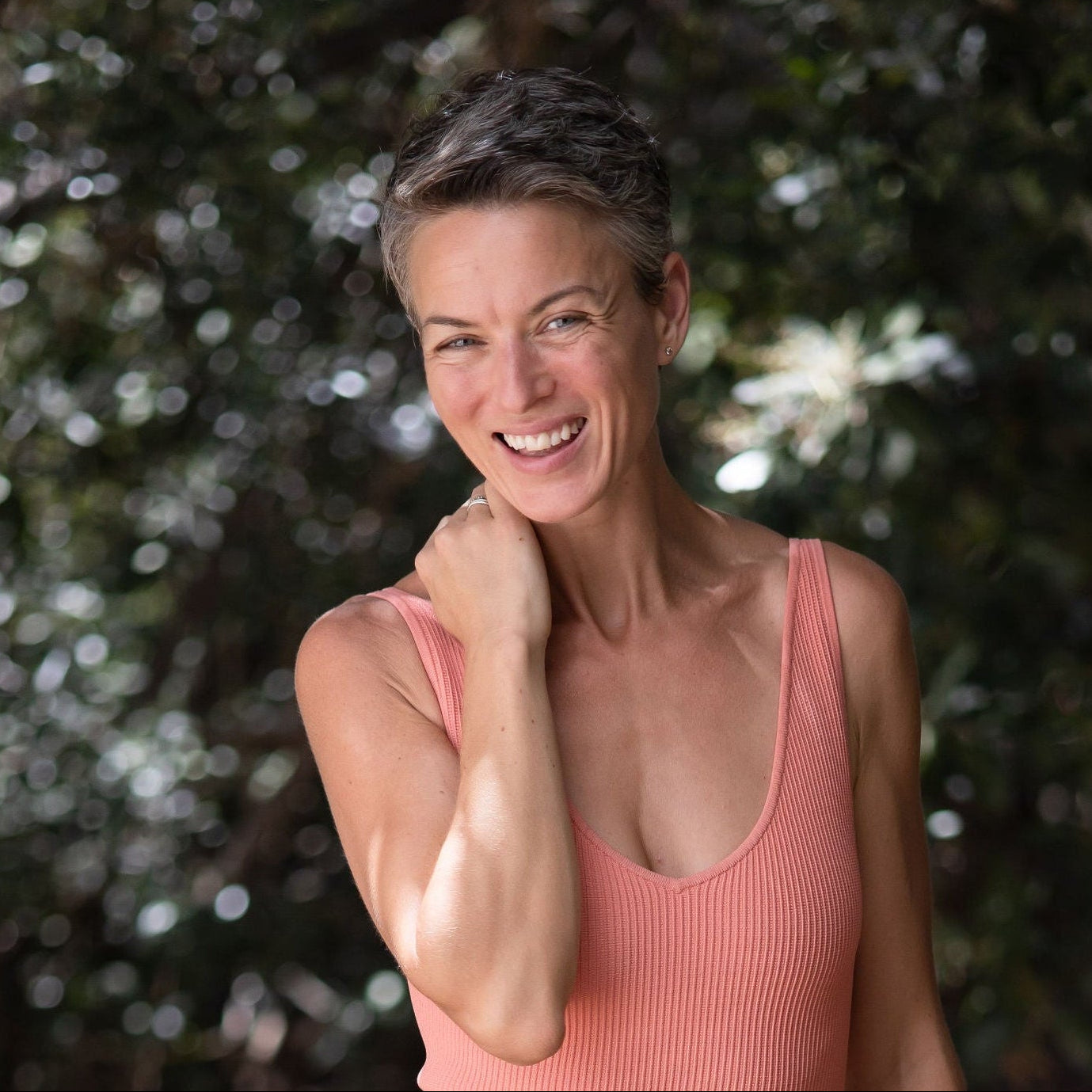 Woman in a pink tank top smiling outdoors with trees in the background