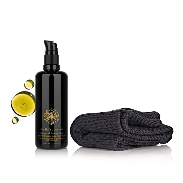 Black bottle with gold design and a dark gray towel on a white background