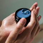 Hand holding a small container of the blue cocoon balm