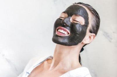 Woman applying a black facial mask with a white background