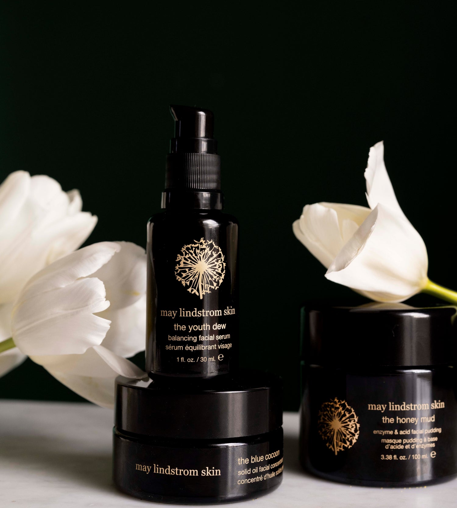May Lindstrom skincare products with white flowers on a dark background