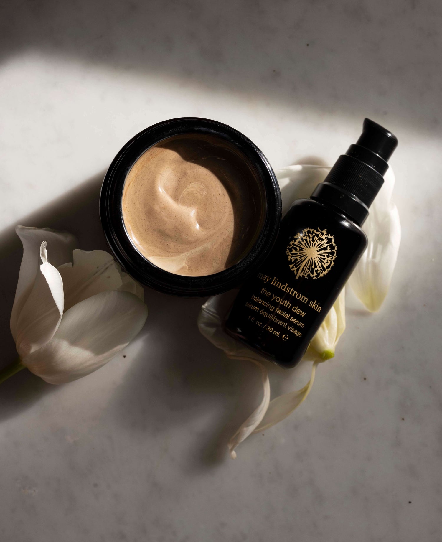 May Lindstrom Skin products including a black container and a bottle with a brand logo on a light background.